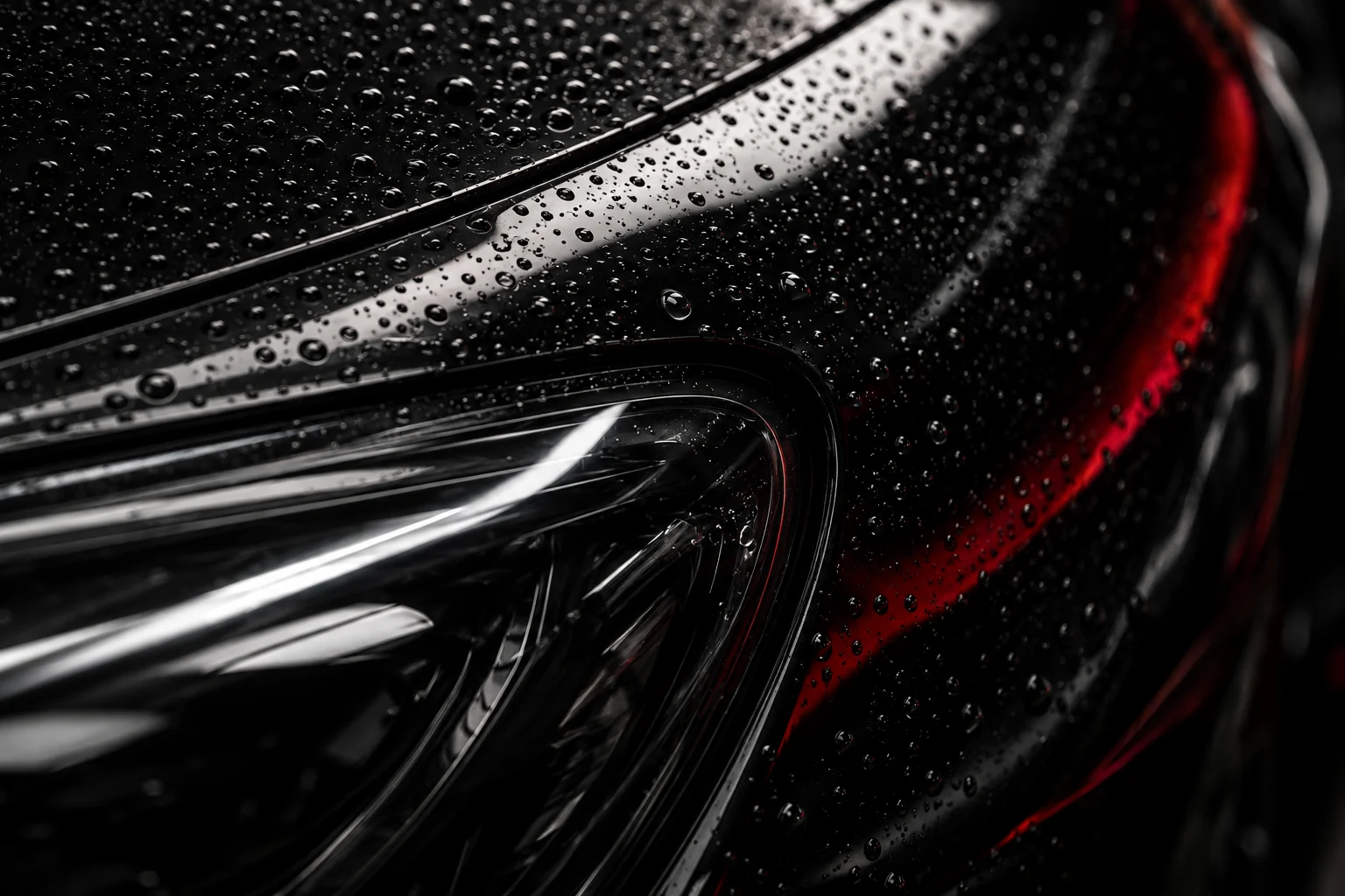 Gouttes sur une carrosserie noire aux reflets rouges, photographie d’ambiance